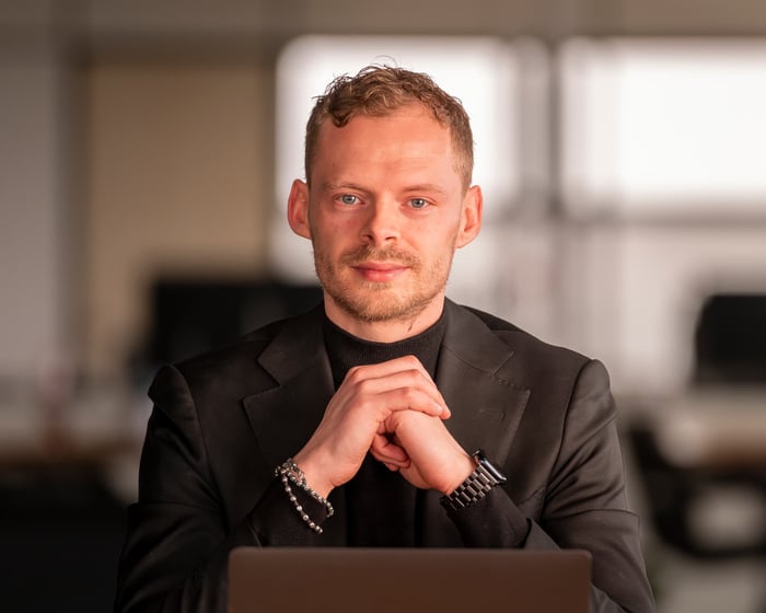 Robin Visser aan zijn bureau in een donker pak, handen gevouwen, kijkend in de camera.